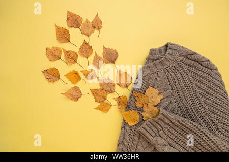 Herbst Zusammensetzung der Blätter und einen warmen Pullover. Flach. Gelber Hintergrund. Herbst Konzept. Stockfoto