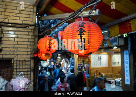 Taipei, Taiwan: Rote Lampions mit der chinesischen Schrift am Dach über dem Bürgersteig in Jiufen Old Street mit verschwommenen Hintergrund Stockfoto