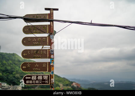 Jiufen, Taiwan: Alte braune metal Richtung Schildern zu den berühmten Sehenswürdigkeiten in Jiufen, Keelung mit dunklen Wolken im Hintergrund Stockfoto