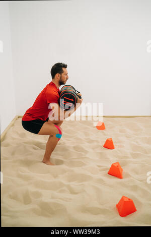 Seitenansicht eines Jungen tragen eine schwarze Tasche auf Sand und eine weiße Wand im Hintergrund. Konzept der Muskel Gesundheit und Entspannung. Bild vertikal Stockfoto