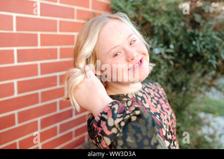 Smiling teenage Mädchen mit Down-syndrom flips Haar draußen in der Sonne Stockfoto