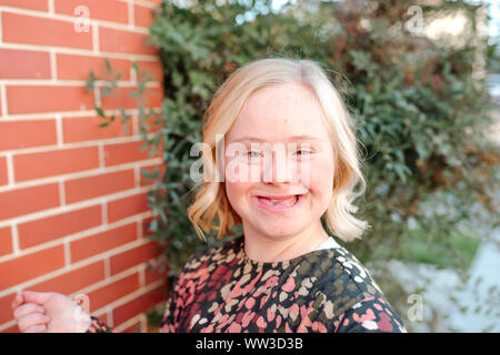 Gerne jugendlich Mädchen mit Down-syndrom lächelnd durch die Mauer an einem sonnigen Tag Stockfoto