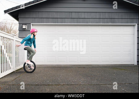 Junge Mädchen reiten Einrad in Einfahrt an einem bewölkten Tag Stockfoto