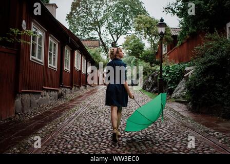 Frau zu Fuß auf einer gepflasterten Straße mit einem Regenschirm in der Regen Stockfoto