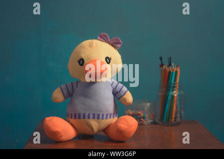 Gefüllte Ente, Spielzeug für Kinder und Babys auf braunen Schreibtisch aus Holz mit blauem Hintergrund. Stockfoto