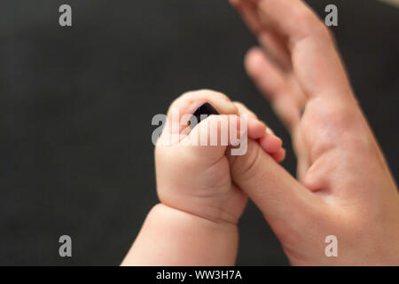 Kid's Hand hält die Finger der Hand seiner Mutter auf schwarzem Hintergrund Stockfoto