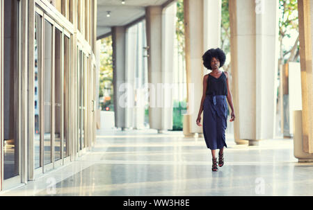 Eine junge Modische afroamerikanischen Frau selbstbewusst hinunter die Halle außerhalb der Gebäude Stockfoto