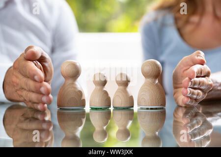 In der Nähe von Paar schützende Hand Holz- Bauer Familie auf reflektierenden Schreibtisch Stockfoto