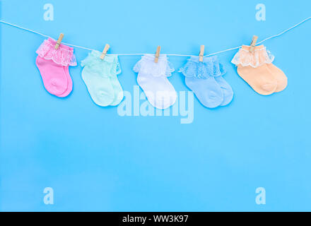 Bunt süß Baby Socken hängen auf der Wäscheleine auf blauem Hintergrund. Baby Accessoires. Flach. Stockfoto