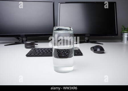 Glas von reinem Wasser mit Computer Desktop auf weißem Schreibtisch Stockfoto