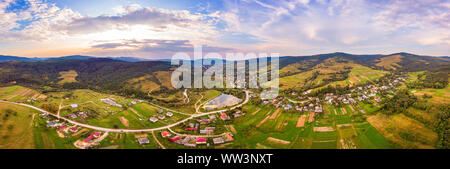 Antenne drone Ansicht der städtischen Dorf Pidbuzh in den Karpaten, in der Ukraine. 180 Grad Panoramablick auf die Landschaft des ländlichen Raums. Sonnenuntergang, Ende des Sommers. Stockfoto