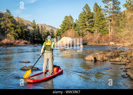 Ältere männliche Paddeln aufblasbare Stand up paddleboard durch Rock Garden auf einem Berg River - Poudre RIver in den Colorado im Frühjahr Landschaft mit niedrigen Wat Stockfoto