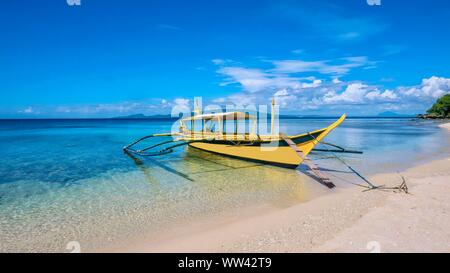 Eine wunderschöne tropische Insel Szene mit einem traditionellen philippinischen Holz- auslegerboot als Banca, in klarem seichten türkisblauen Wasser auf einem whi verankert Stockfoto