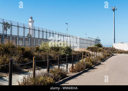 Grenzzaun zwischen San Diego und Tijuana, Mexiko, mit El Faro de Tijuana Leuchtturm auf die Mexiko Seite und einen Turm. Stockfoto