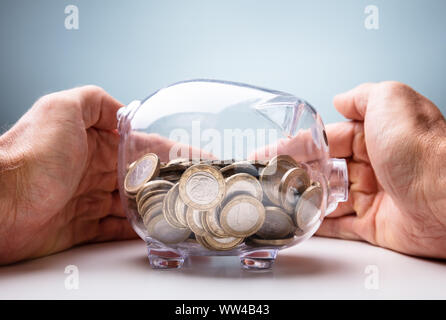 Mittelteil der Geschäftsfrau Schutz der Münzen in transparenten Sparschwein an den hölzernen Tisch Stockfoto