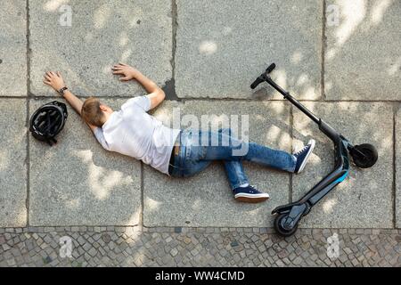 Unbewussten Mann liegen auf konkrete Straße nach Unfall mit einem Elektroroller Stockfoto