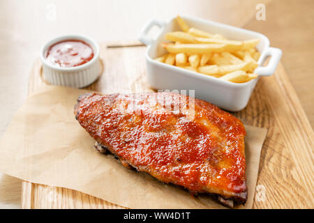 Leckere Rippchen. Full Rack der RIBS BBQ auf Holzplatte mit Pommes Frites und Salat Stockfoto
