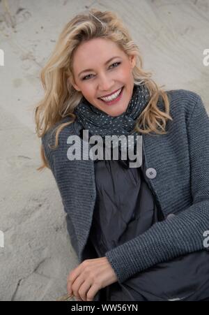 Attraktive Frau im Sand liegend tragen eine Strickjacke Stockfoto