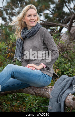 Frau sitzt lächelnd auf umgefallene Baum Stockfoto