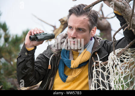 Mann mit Fernglas und gelben Pullover etwas beobachten Stockfoto