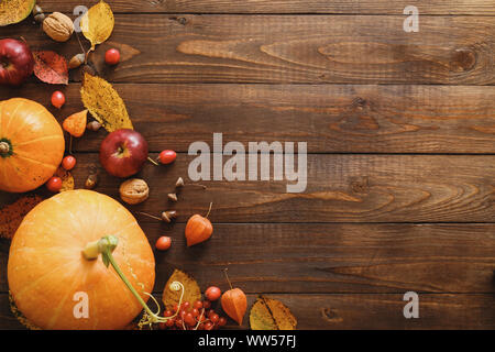 Kreative, oben flach Herbst Komposition. Umrandung aus Kürbissen, getrocknet fallen Blätter, rote Beeren, Äpfel, Walnüsse auf Holz- Hintergrund. Th Stockfoto