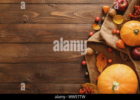 Ernte oder Thanksgiving Hintergrund mit Kürbissen, Decke, getrocknet Herbstlaub, Äpfel, rote Beeren, Walnüsse auf hölzernen Tisch. Flach Zusammensetzung, oben Stockfoto