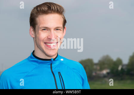 Mann in blauem Trainingsanzug top lächelnd, an der Kamera suchen, Porträt Stockfoto