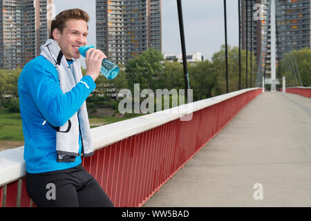 Mann in blauem Trainingsanzug top und Handtuch an der Balustrade, Sport, Pause, Trinkflasche Stockfoto