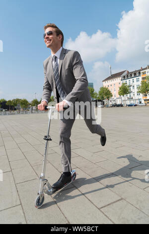 Mann im grauen Anzug geht Reiten Roller Stockfoto