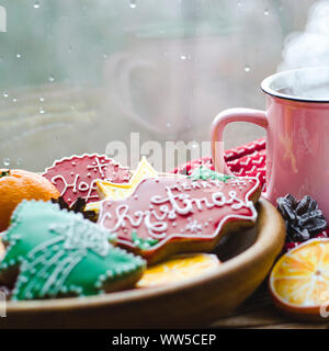 Eine heiße Tasse Tee steht auf einem hölzernen Tisch neben einem hölzernen Platte auf die Lebkuchen Cookies von orange Schnitte vor dem Hintergrund einer Stockfoto