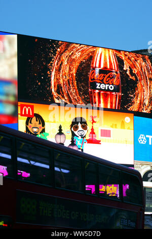 Ein roter Doppeldeckerbus Fahren hinter einem großen ad Box auf dem Piccadilly Circus in London, Stockfoto