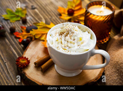 Pikante Kürbis Latte mit Schlagsahne. Herbst Kaffee Tasse mit Kürbis und Zimt Gewürz auf Holztisch mit Herbst Kerzen und Dekoration noch Leben Stockfoto