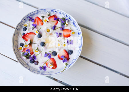 Joghurt mit Erdbeeren, Heidelbeeren und Blüten auf Weiß Holztisch Stockfoto