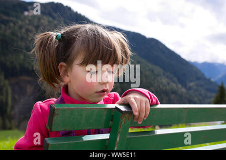 4-6 Jahre altes Mädchen mit Zöpfen sitzen auf der grünen Bank Stockfoto