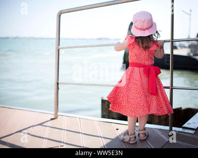 4-6 Jahre altes Kind im roten Kleid an der Anlegestelle wartet Stockfoto