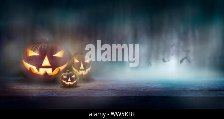 Jack O'Lanterns auf einer Bank in einem kalten Nebel, nebligen Wald bei Nacht mit Fledermäusen im Hintergrund. Stockfoto