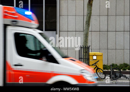 Fotografie von abgestellte Fahrräder und Motorroller vor eine Mailbox mit einem Krankenwagen mit Blaulicht fahren, Stockfoto