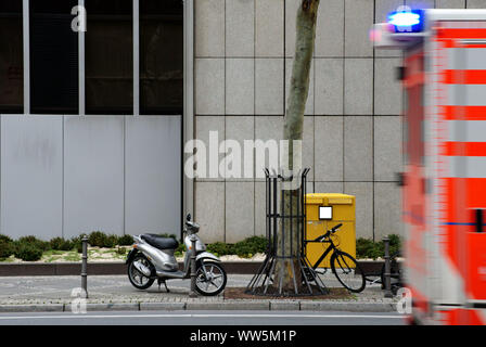 Fotografie von abgestellte Fahrräder und Motorroller vor eine Mailbox mit einem Krankenwagen mit Blaulicht fahren, Stockfoto