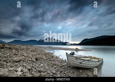 Boot am Ufer des Walchensee kurz nach Sonnenuntergang. Im Hintergrund der Münchner Hinterhof berge Herzogstand, Heimgarten und Jochberg und eine Halbinsel von Kies, in zwischen der Insel Sassau. Stockfoto