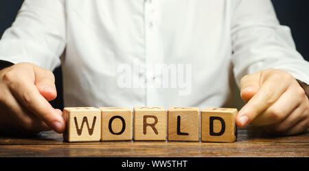Ein Mann legt Holzblöcke mit dem Wort Welt. Der Begriff der Globalisierung und globalen Unternehmen. Internationale Beziehungen. Diplomatie. Investitionen Stockfoto