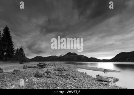 Boot am Ufer des Walchensee kurz nach Sonnenuntergang. Im Hintergrund der Münchner Hinterhof berge Herzogstand, Heimgarten und Jochberg und eine Halbinsel von Kies, b/w Stockfoto