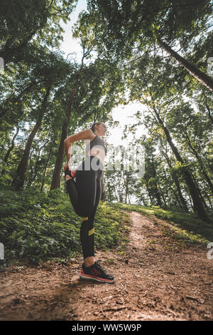 Low Angle Image der jungen Sportlerin und Warm-up vor dem Training im Wald. Seitenansicht des slim fit female Vorbereitung auf den Waldweg zu starten Stockfoto