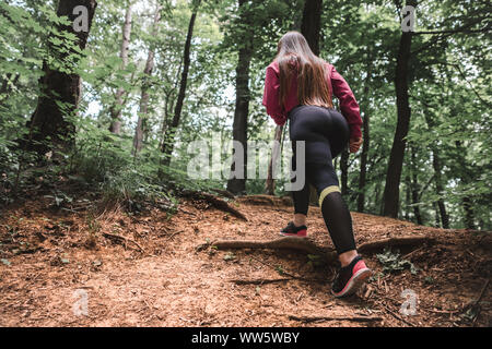 Volle Länge schossen junge sportliche Mädchen überwindet steile für die Ausbildung in den Wald klettert. Rückansicht eines überzeugten weiblichen Athleten Klettern ein Waldweg. Stockfoto