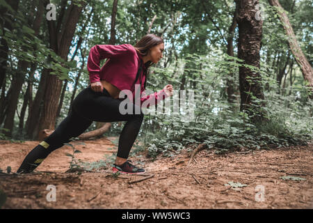 Seitenansicht eines junge sportliche Mädchen überwindet steile für die Ausbildung in den Wald klettert. Volle Länge geschossen von einer selbstbewussten weiblichen Athleten Klettern ein Wald tr Stockfoto