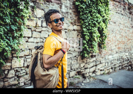 Cute hübscher junger Mann im gelben T-Shirt mit einer modischen Frisur posiert in der Nähe von einer alten Steinmauer. Indische attraktiver Kerl Modell restin Stockfoto