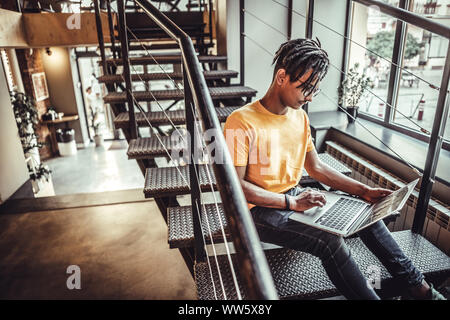 Auf der Arbeit konzentriert. Seitenansicht des selbstbewussten jungen Mann in Brillen Arbeiten am Laptop während im Büro oder im Café sitzen. Stockfoto