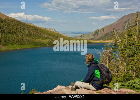 Junger Mann auf einem Stein saß und mit Blick auf den Bergsee im Tal, Rocky Mountains, Alberta, Kanada Stockfoto