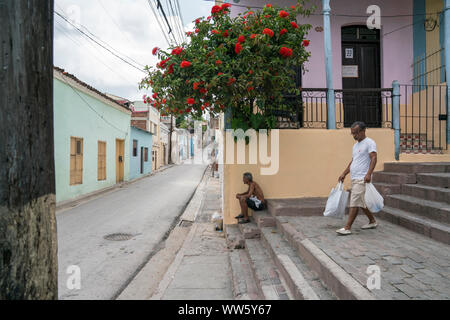 Ein Mann sitzt auf der Treppe in Santiago de Cuba, einem anderen hinunter mit Käufen, Häuser, einen Balkon mit Blumen, eine Straße, Gebäude mit Kabel Stockfoto