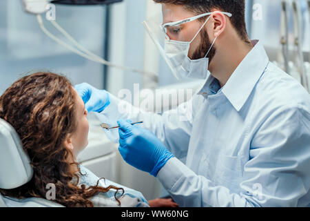 Zahnarzt sehr sorgfältig prüfen und Zahn seine junge Patientin reparieren. Von der Seite. Stockfoto