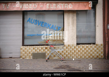 Ein leerer Warenkorb auf dem Bürgersteig vor einem geschlossenen elektrischen waren Shop mit zerbrochenen Fensterscheibe, Stockfoto